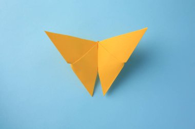 Origami sanatı. Açık mavi zemin üzerinde el yapımı sarı kağıt kelebek, üst görünüm