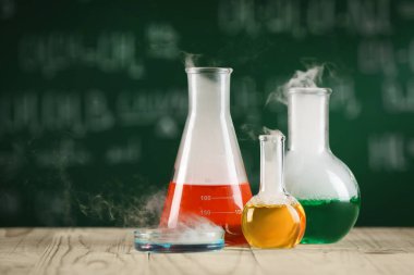 Laboratory glassware with colorful liquids on wooden table, space for text. Chemical reaction