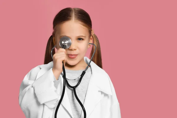 Pembe Arka Planda Steteskobu Olan Tıp Üniformalı Küçük Bir Kız — Stok fotoğraf