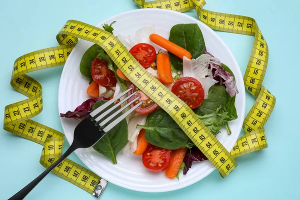 测量带子 蔬菜色拉和叉子 浅蓝色底色 体重减轻概念 — 图库照片
