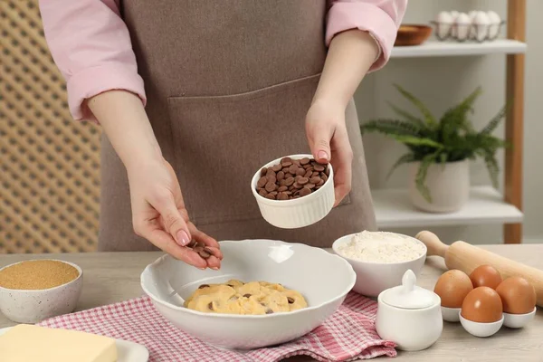 Cooking sweet cookies. Woman adding chocolate chips to dough at table in kitchen, closeup