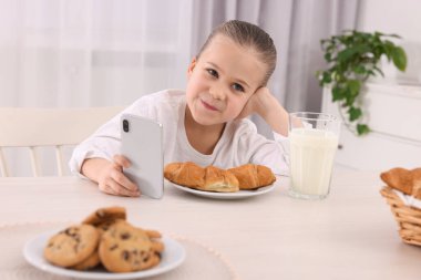 İçeride kahvaltı ederken akıllı telefon kullanan küçük bir kız. İnternet bağımlılığı