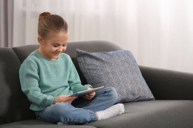 Evdeki kanepede tablet kullanan küçük bir kız. İnternet bağımlılığı