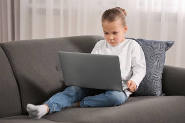 Evdeki kanepede dizüstü bilgisayar kullanan küçük bir kız. İnternet bağımlılığı