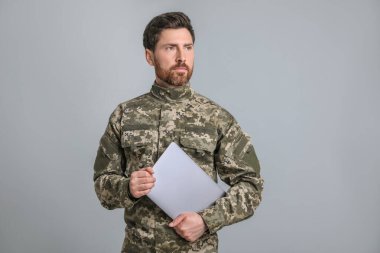 Açık gri arka planda dizüstü bilgisayarı olan asker. Askerlik.
