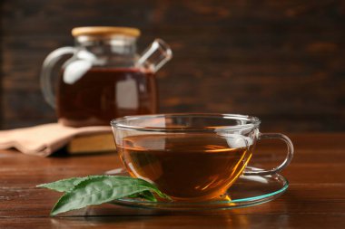 Bir fincan aromatik çay, yeşil yapraklar ve çaydanlık ahşap masada, yakın plan.