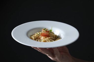 Elinde jambonlu lezzetli spagetti tabağı ve siyah arka planda mikroyeşillikler olan bir kadın, yakın plan. Makarna yemeğinin enfes sunumu