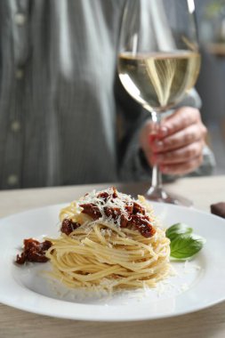 Restorandaki ahşap masada güneşte kurutulmuş domatesli, parmesan peynirli ve şaraplı leziz spagetti yiyen bir kadın. Yakın plan. Makarna yemeğinin enfes sunumu