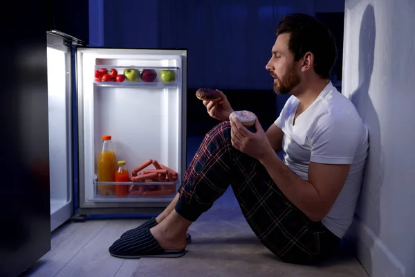 一个晚上在厨房冰箱边拿着甜甜圈的人 坏习惯 — 图库照片
