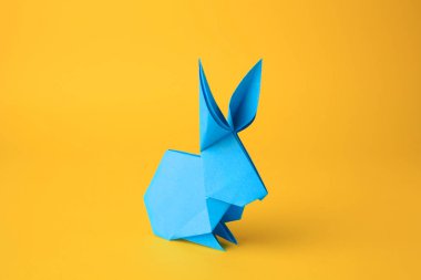 Origami sanatı. Sarı arkaplanda el yapımı açık mavi kağıt tavşan, yakın plan.