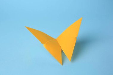 Origami sanatı. Açık mavi arkaplanda el yapımı sarı kağıt kelebek