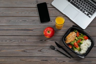 Lezzetli yemek kabı, bir bardak meyve suyu, laptop, elma ve akıllı telefon ahşap masada, mesaj için yeri olan düz bir yer. İş yemeği.
