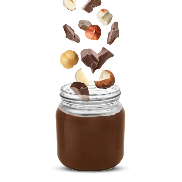 Making yummy chocolate paste. Hazelnuts and pieces of chocolate falling into jar on white background