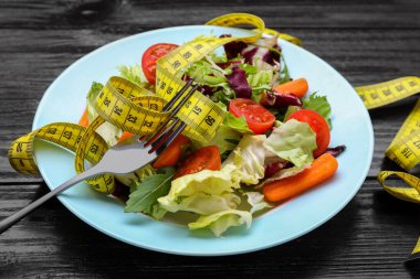 Tabak taze sebze salatası, çatal ve mezura ile ahşap masa, yakın plan. Sağlıklı diyet kavramı