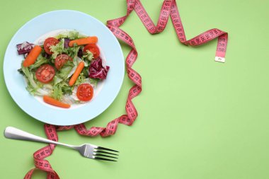 Açık yeşil arka planda taze sebze salatası, çatal ve mezura tabağı, metin için boşluk. Sağlıklı diyet kavramı