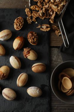 Taze pişirilmiş ev yapımı ceviz şekilli kurabiyeler ve ahşap masada fındıklar.