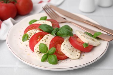 Domatesli Caprese salatası, mozzarella, fesleğen ve baharatlar beyaz masada, yakın plan.