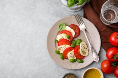 Domatesli Caprese salatası, mozzarella, fesleğen ve baharatlar açık gri masada servis edilir. Metin için boşluk