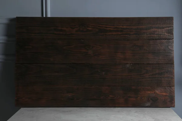 Dark wooden board on table near light grey wall