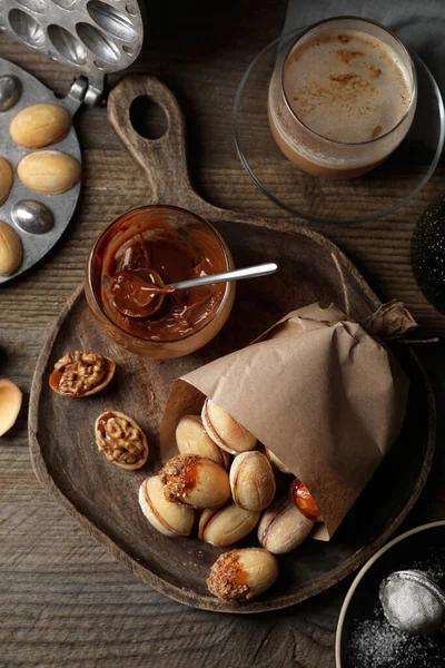 stock image Freshly baked homemade walnut shaped cookies, boiled condensed milk and cup of coffee on wooden table, flat lay