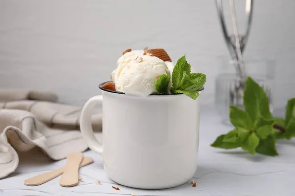 Scoops of ice cream with caramel sauce, candies and mint leaves on white textured table, closeup