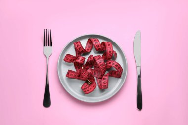 Mezura, çatal ve bıçak pembe arka planda, düz yerde. Kilo verme konsepti
