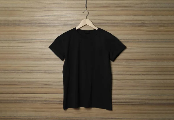 木の壁にスタイリッシュな黒のTシャツでハンガー — ストック写真