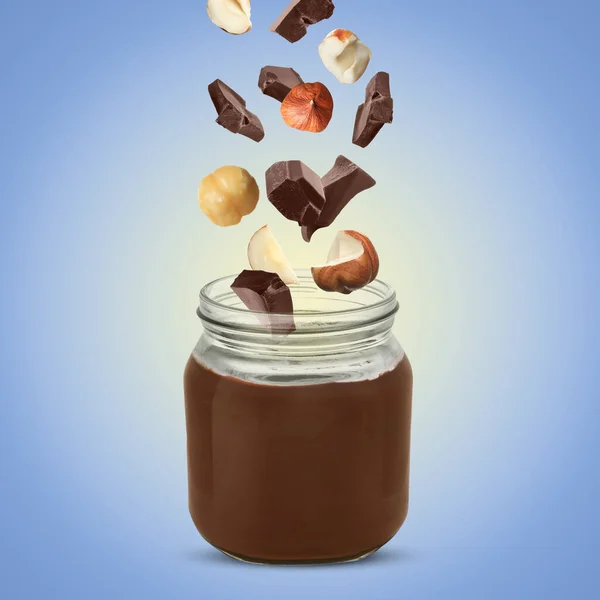 Making yummy chocolate paste. Hazelnuts and pieces of chocolate falling into jar on light blue background