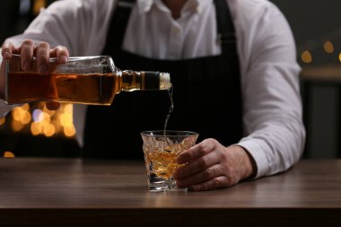 Barmen bardaki tezgahta şişeden cama viski dolduruyor, yakın plan.