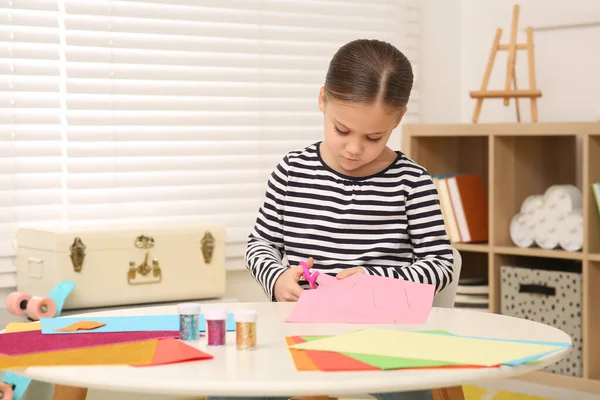 かわいい女の子が部屋の机でピンクの紙を切っている ホームワーク — ストック写真