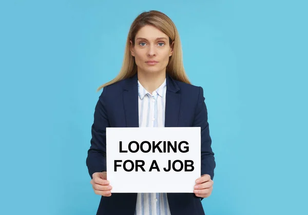 拿着写着 寻找浅蓝色背景工作 字样的失业妇女 — 图库照片