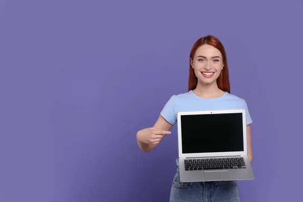 在淡紫色背景上展示笔记本电脑的年轻女性微笑 文字空间 — 图库照片