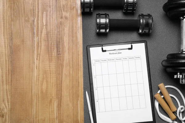Personal training. Clipboard with workout plan and sports equipment on wooden table, flat lay. Space for text