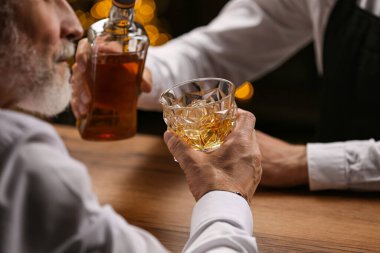 Barmen bardaki müşteriye bardağa viski dolduruyor.