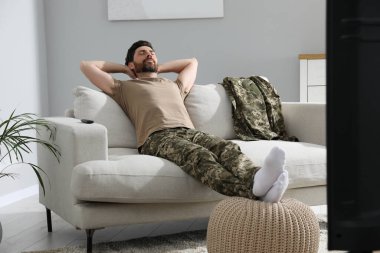 Oturma odasındaki TV 'nin yanındaki yumuşak kanepede uyuyan asker. Askerlik.