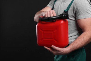 Man holding red canister on black background, closeup. Space for text