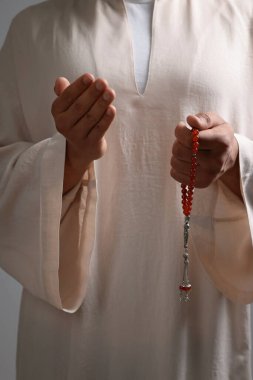 Misbaha 'lı Müslüman bir kadın açık gri arka planda dua ediyor, yakın plan
