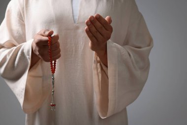 Misbaha 'lı Müslüman bir kadın açık gri arka planda dua ediyor, yakın plan