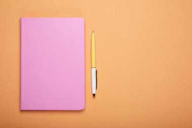 Kapalı pembe defter ve soluk turuncu arka planda kalem, düz. Metin için boşluk