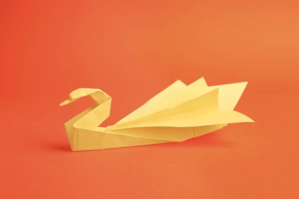 Origami art. Paper swan on orange background,