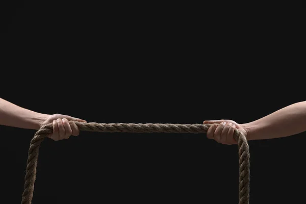 Dispute concept. Men pulling rope on black background, closeup. Space for text
