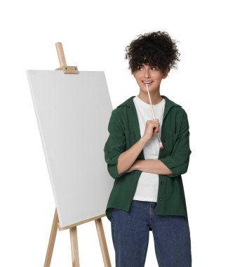Beyaz arka planda tuval ile sehpanın yanında fırça tutan genç bir kadın.