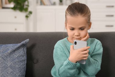 Evdeki kanepede akıllı telefon kullanan küçük bir kız. İnternet bağımlılığı