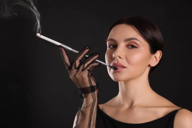 Siyah arka planda sigara içmek için uzun sigara tutacağı kullanan kadın.