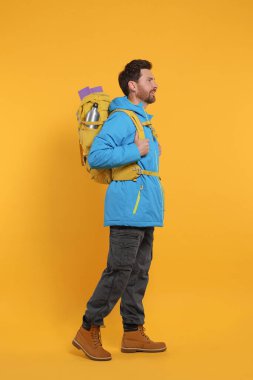 Sırt çantalı bir adam turuncu arka planda yürüyor. Etkin turizm