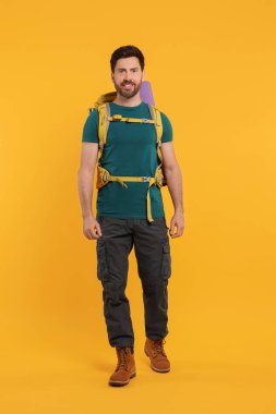 Turuncu arka planda sırt çantalı mutlu bir adam. Etkin turizm