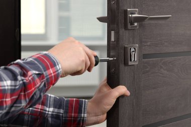 Handyman with screwdriver repairing door lock indoors, closeup clipart