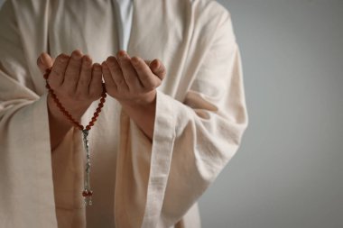 Misbaha 'lı Müslüman bir adam açık gri arka planda dua ediyor, yakın plan. Metin için boşluk