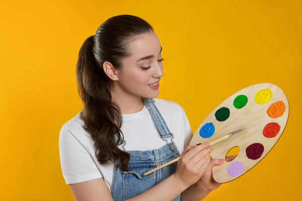 带着黄色背景的绘画工具的女人年轻的艺术家 — 图库照片