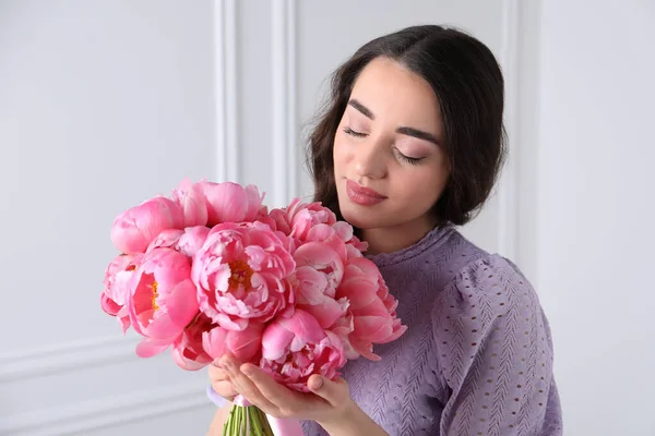 白い壁の近くにピンクの牡丹の花束を持つ美しい若い女性 — ストック写真